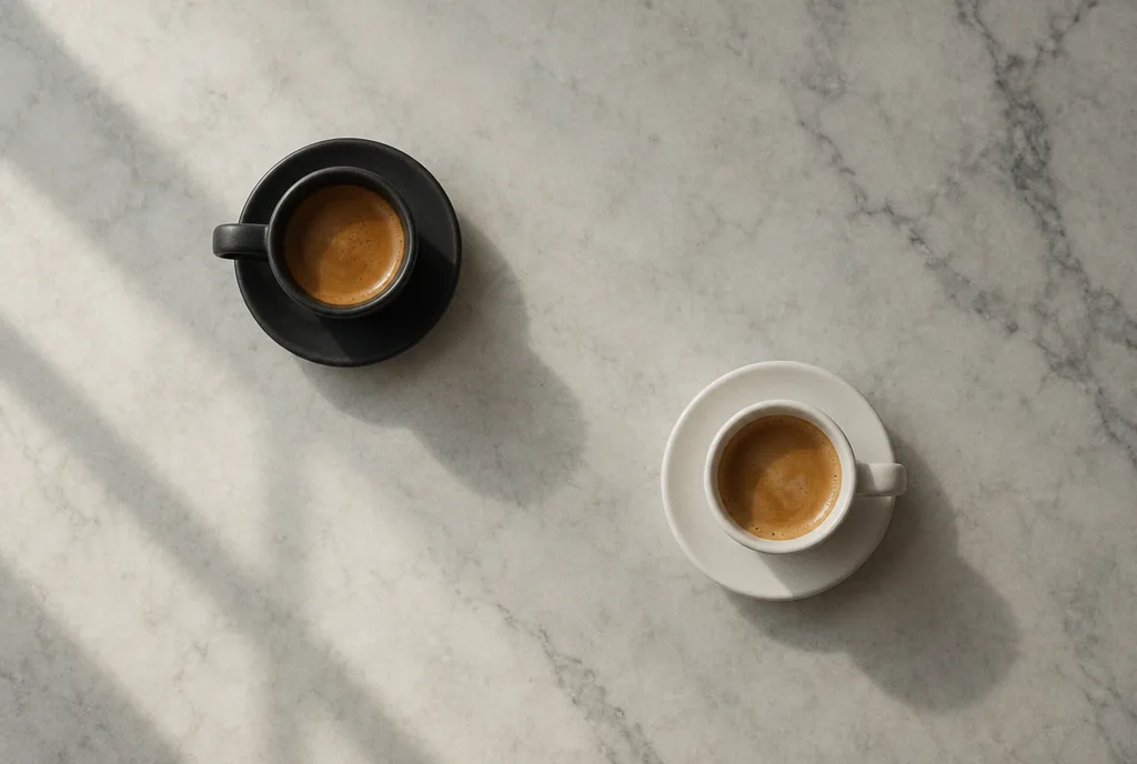 O ceașcă de espresso neagră și una albă pe o masă de marmură, văzute de sus.